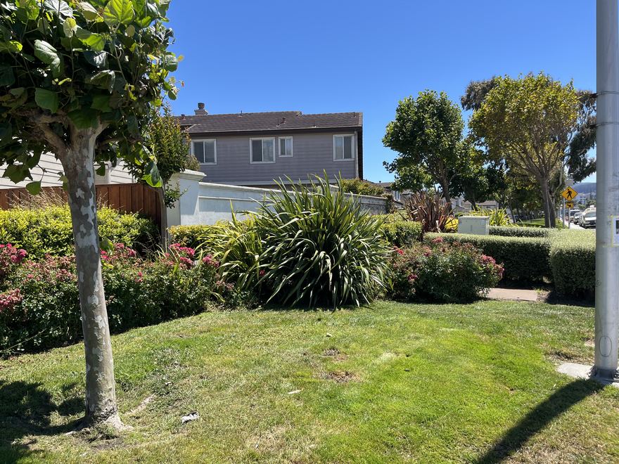 A grassy landscaped corner in ParcPlace bordered by flowering shrubs, with homes behind.