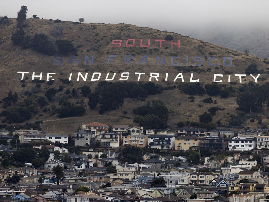 The South San Francisco hillside sign reading &ldquo;The Industrial City&rdquo; rising above the ParcPlace neighborhood rooftops.